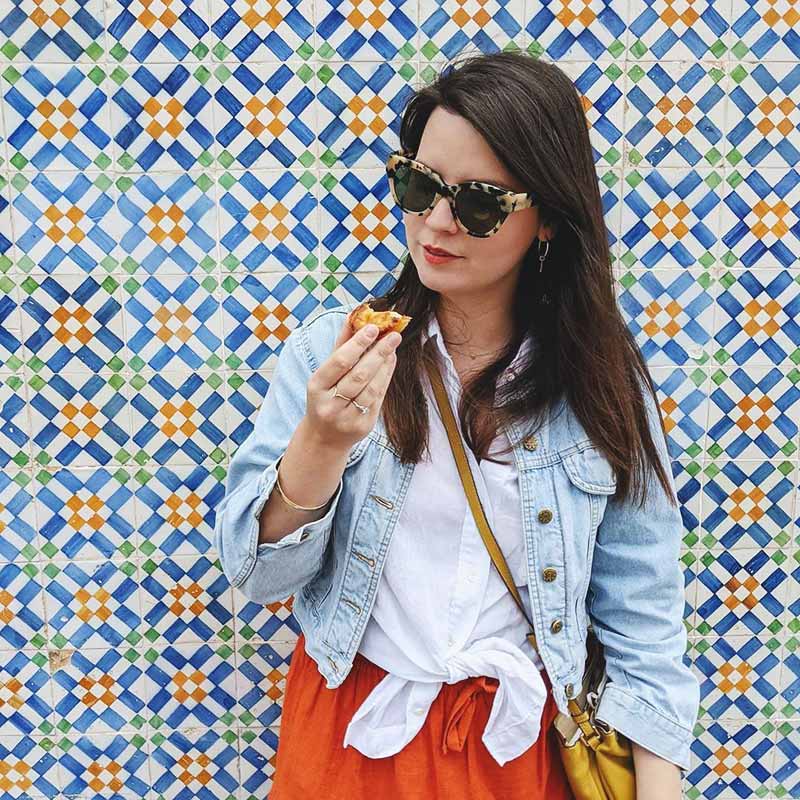 Daniela Sunde-Brown eating a pastel de nata against a tiled wall
