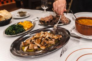 A hand sticking a fork into a plate of pork belly at Rui Manel dos Ossos in Coimbra